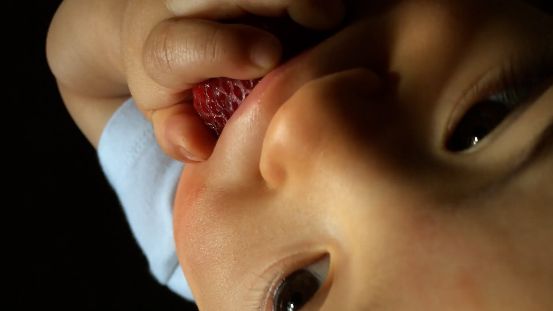 Nesting — video still, strawberry Close-up video still from Nesting showing a baby holding a strawberry near their mouth.