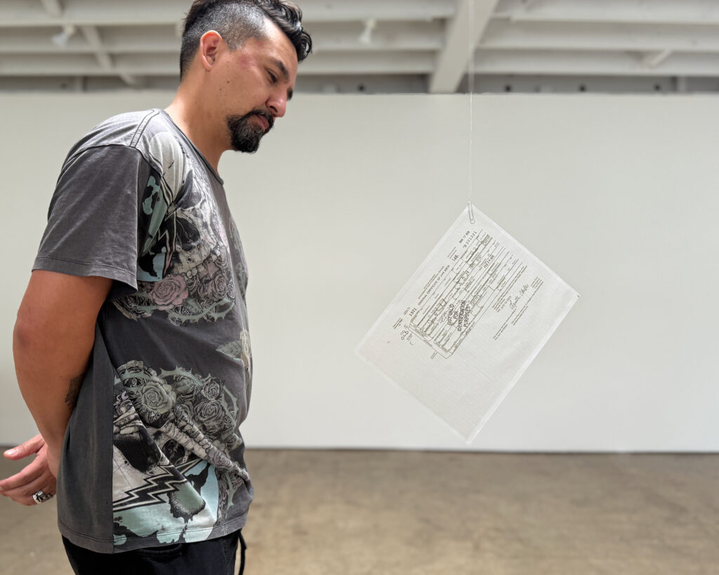 Not Valid for Identification Purposes — installation view with viewer, 2025 Viewer standing beside Not Valid for Identification Purposes, a letter-sized vellum document suspended from monofilament.